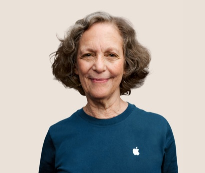 Retrato de una persona del equipo de Apple Retail sonriendo con cabello ondulado, gris oscuro.