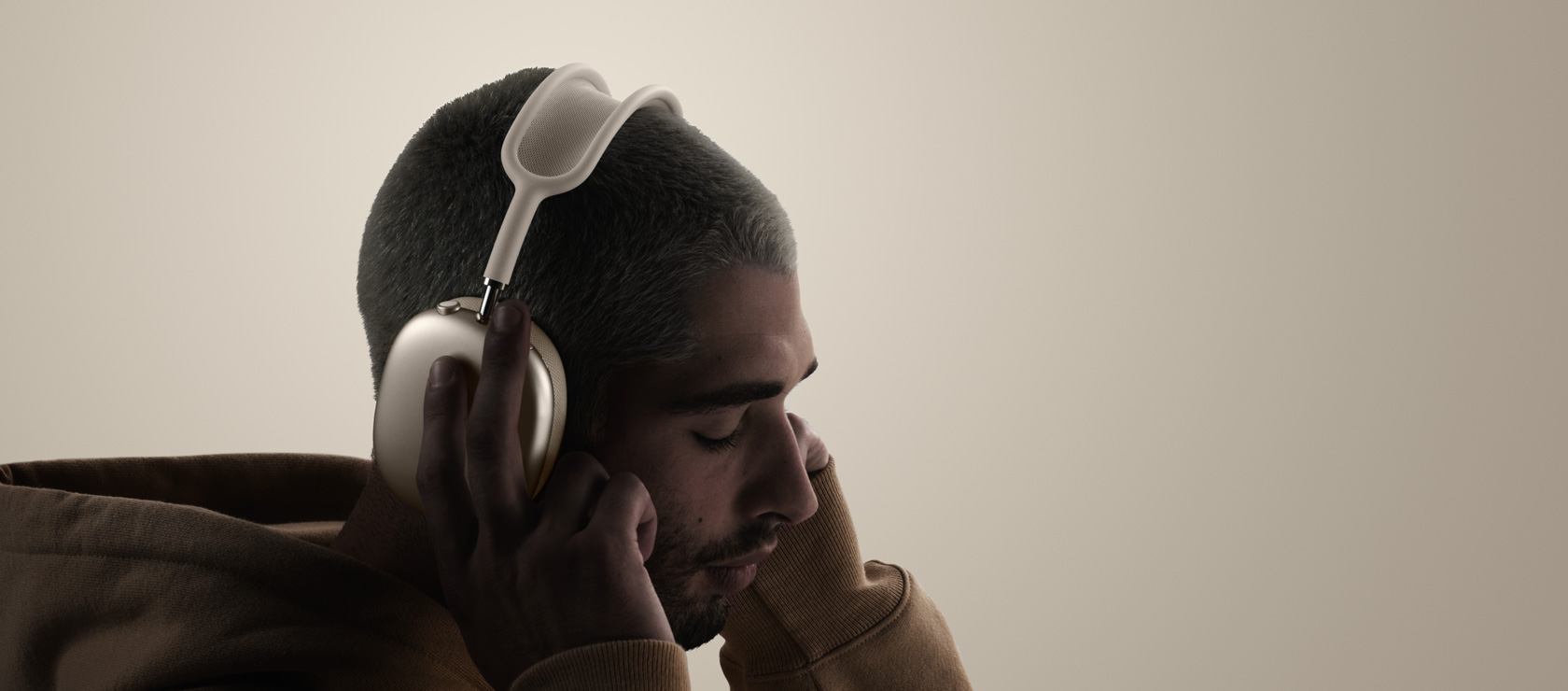 Άτομο που φοράει ακουστικά AirPods Max 2, πλαϊνή εξωτερική όψη, αγγίζει τα μαξιλαράκια ακουστικών