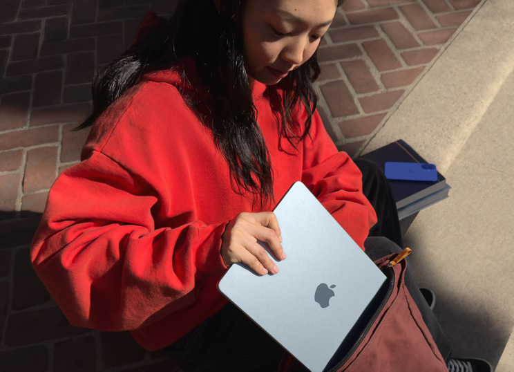 Una persona sentada en unos escalones de piedra pone su MacBook en una mochila.