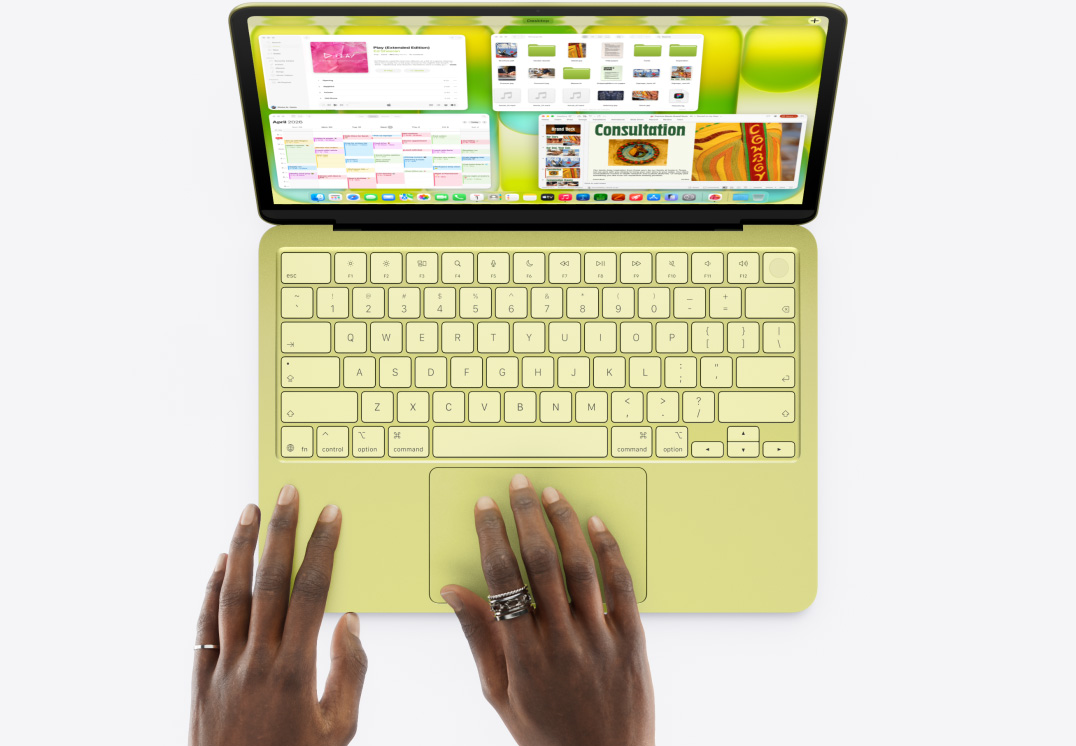 MacBook Neo, Farbe Zitrus, eine Hand auf dem Trackpad, mehrere Fenster geöffnet, darunter die Apps Musik, Kalender und Microsoft PowerPoint