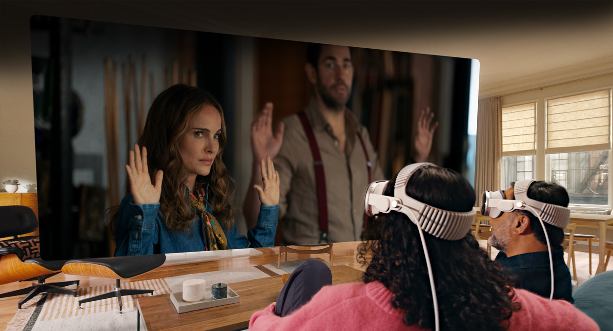 Two people both wearing Apple Vision Pro sit side by side on sofa watching Fountain of Youth movie, displayed on screen stretching across room